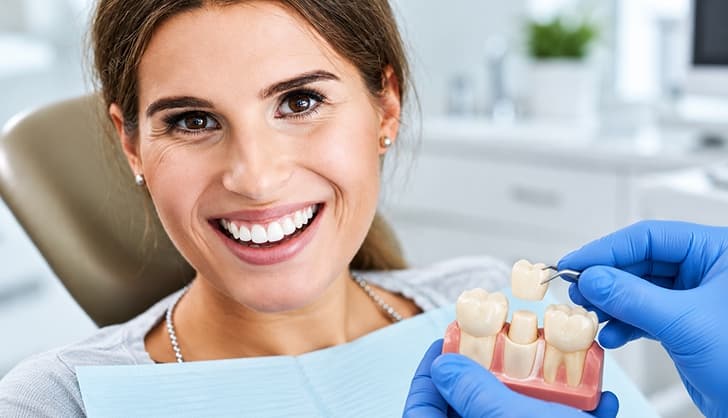 Smiling patient viewing a dental crown and bridge model